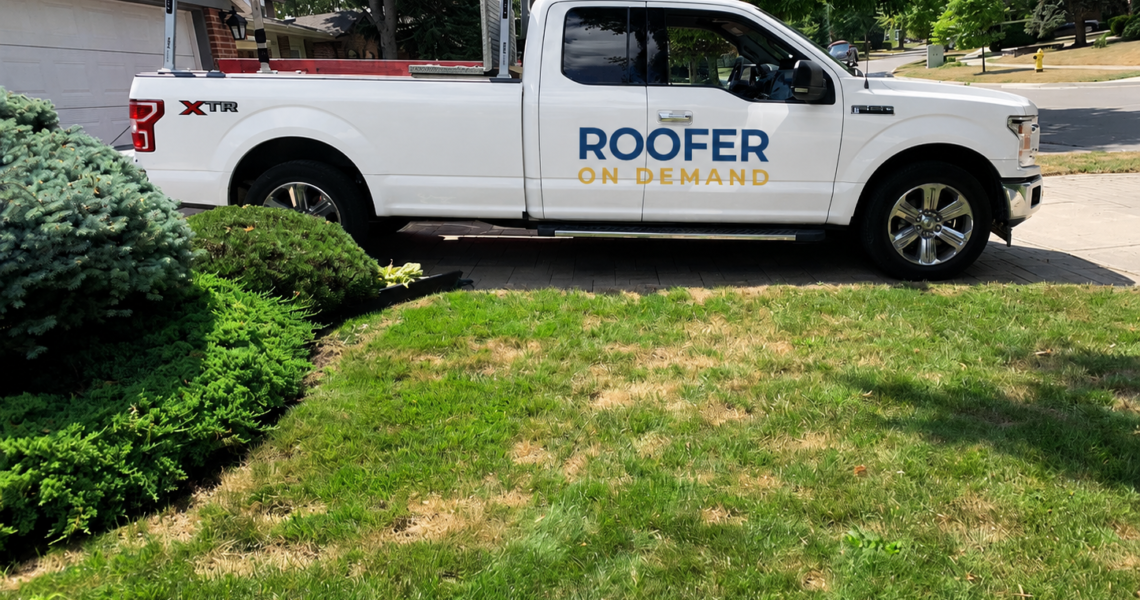 A white pickup truck with Roofer On Demand written on the side, offering water damage restoration Toronto, is parked in a driveway next to a green lawn and shrubs in a suburban neighborhood.