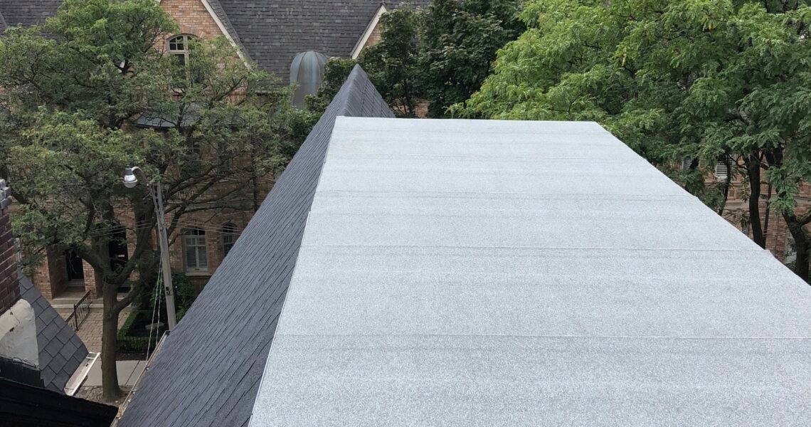 View from a rooftop with a light gray, flat surface—ideal for water damage restoration Toronto—overlooking nearby trees, older brick buildings, and tall modern apartment buildings in the background under a cloudy sky.